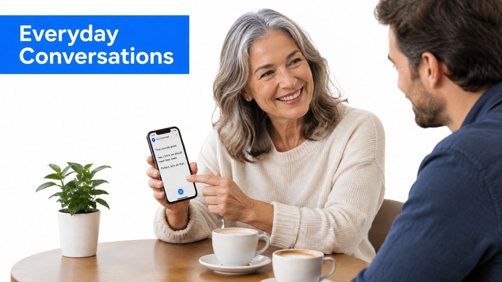 A woman with grey hair smiles while showing a smartphone with live transcription to a man.